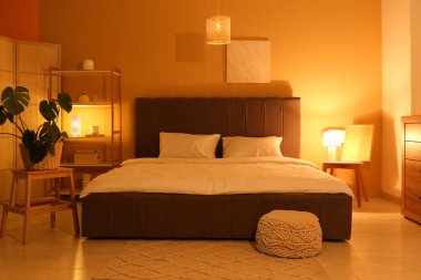 Gece yatak odasının içinde büyük bir yatak odası, raf ünitesi, katlanan ekran ve sarı duvarın yanında parlayan lambalar.