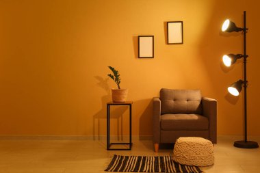 Gece oturma odasının içinde, koltuğu, parlak lambaları ve sarı duvarın yanındaki taburede bulunan çiçeklerle.