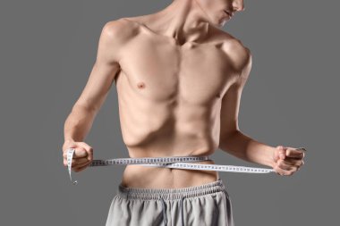 İştahsızlığı olan genç bir adam, gri arka planda belini ölçüyor.