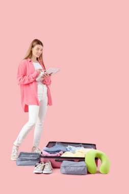 Pembe arka planda bavul hazırlayan listedeki kadın turist.