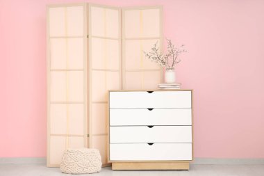 Katlanan ekran ve çiçek açan ağaç dalları pembe duvarın yanındaki şifoniyerde.