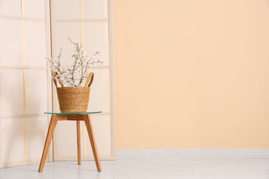 Katlanan ekran ve çiçek açan ağaç dalları bej duvarın yanındaki cam sehpanın üzerinde.