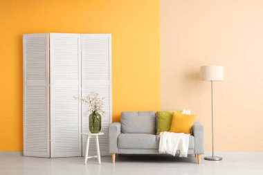 Gri kanepeli, katlanır perdeli ve sehpanın üzerinde çiçek açan ağaç dalları olan şık bir oturma odası.