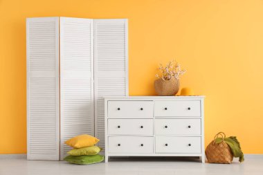 Katlanmış perdeli şık bir oda ve şifoniyerin üzerinde çiçek açan ağaç dalları.