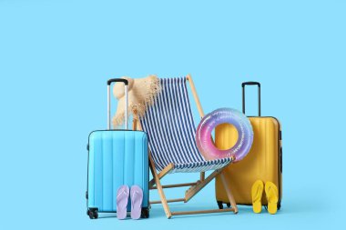 Çizgili güverte sandalyesi şişirilebilir yüzük, parmak arası terlik ve mavi arka planda bavullar.