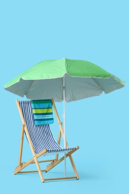 Mavi arka planda havlu ve şemsiyeli çizgili iskemle.