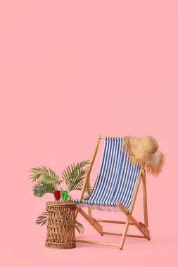 Çizgili güverte sandalyesi ve pembe arka planda kokteyl bardaklarıyla hasır masa.