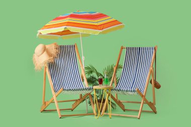 Yeşil arka planda şemsiyeli çizgili güverte sandalyeleri ve kokteyl bardakları