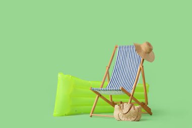 Plaj çantalı çizgili sandalye ve yeşil arka planda şişme yatak.