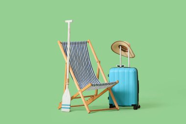 Yeşil arka planda kürek ve bavullu çizgili iskemle.