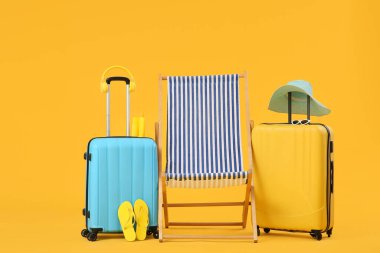 Bavullu çizgili iskemle ve sarı arka planda parmak arası terlik