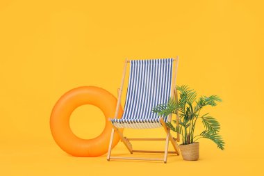 Çizgili güverte sandalyesi, şişme yüzük ve sarı arka planda palmiye ağacı.