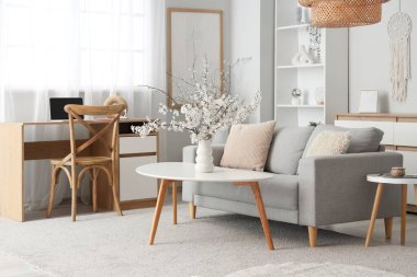 Oturma odasının içinde kanepe, masa ve vazoda çiçek açan dallar var.