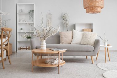 Aydınlık oturma odasının içinde, kanepe ve vazolarda çiçek açan dallar var.