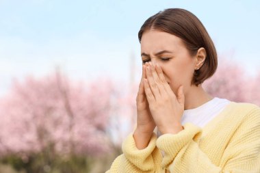 Alerjisi olan genç bir kadın parkta hapşırıyor.
