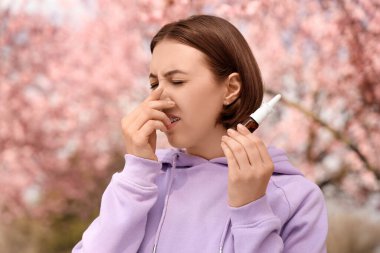 Burnunda damlalar olan alerjik genç bir kadın parkta hapşırıyor, yakın plan.
