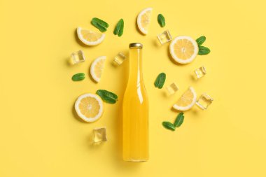 Sarı zemin üzerinde bir şişe içki, limon dilimleri, nane ve buz küpleri olan kompozisyon