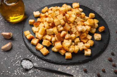 Koyu arka planda kıtır kıtır kızarmış ekmek ve farklı baharatlar olan siyah tahta, yakın plan.