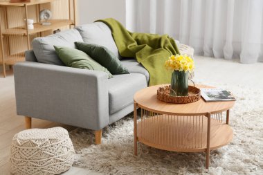 Oturma odasında kahve masası ve narsist çiçekleri olan rahat bir kanepe.