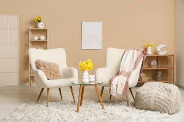 Raf üniteli rahat koltuklar, kahve masası ve bej duvarlı narsis çiçekleri oturma odasında.