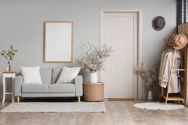 Oturma odasının içinde kanepe, elbise askılığı ve masaların üzerinde vazolar halinde çiçek açan güzel dallar.