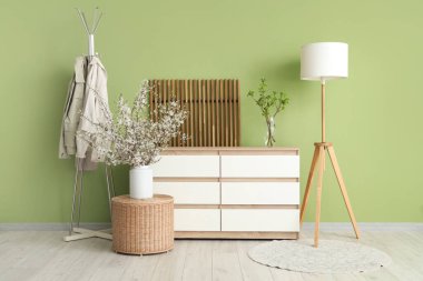 Oturma odasının içinde lamba, giysi askılığı, tuvalet ve hasır masanın üzerinde vazodaki güzel çiçek açan dallar.