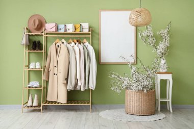 Oturma odasının içinde giysi askılığı ve vazoların üzerinde çiçek açan güzel dallar.