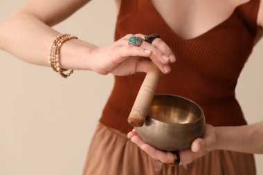 Kadın Tibet müzik kasesiyle meditasyon yapıyor. Bej arka planda, yakın plan.
