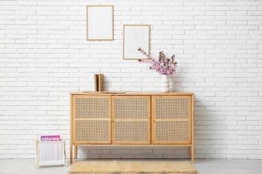 Oturma odasındaki beyaz tuğla duvarın yanında farklı bir dekor ve pembe çiçek açan vazo içeren bir elbise.