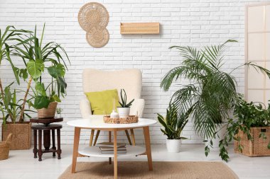 Beyaz tuğla duvarın yanında koltuk, masa ve çiçeklerle dolu bir oda.