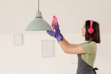 Evde kulaklıklı, lamba temizleyen kadın hademe.