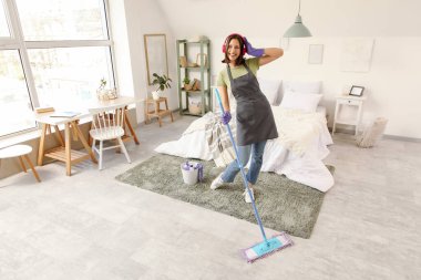 Kulaklıklı kadın hademe yatak odasında yerleri paspaslıyor.