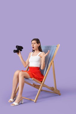 Leylak arka planında güverte sandalyesinde dürbünüyle şok olmuş genç bir kadın.