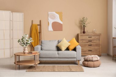 Şifoniyerli kanepe, sehpa ve beyaz çiçekli vazo oturma odasındaki bej duvarın yanında.