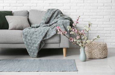 Oturma odasındaki beyaz tuğla duvarın yanında puf ve vazo açan dallarla dolu kanepe.