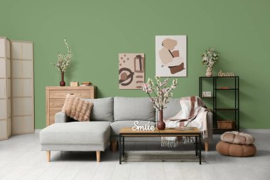 Sehpası, şifoniyeri ve yeşil duvarın yanında çiçek açan vazoları olan bir kanepe.