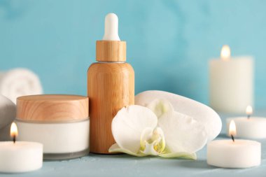 Kozmetik ürünleri, spa taşları ve renkli masada yanan mumlar.