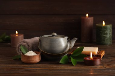 Çaydanlık, kozmetik ürünler ve ahşap masada yanan mumlarla kaplıca bileşimi