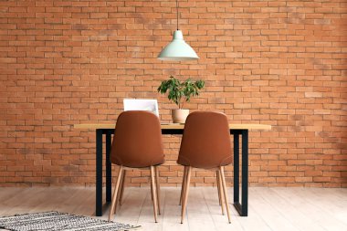 Laptoplu yemek masası ve odada tuğla duvarın yanına bitki.