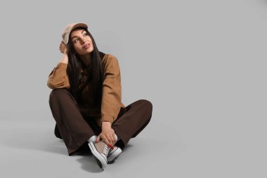 Gri arka planda oturan şapkalı şık genç kadın.