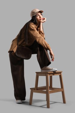 Gri arka planda dışkısı olan şapkalı şık genç bir kadın.