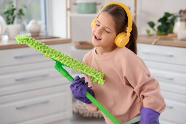 Kulaklıkları ve paspası olan tatlı bir kız mutfakta şarkı söylüyor.