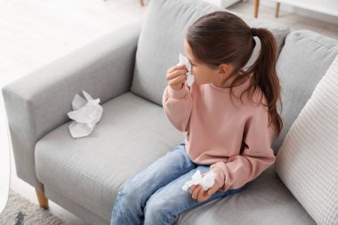 Evdeki koltukta hapşıran peçeteli alerjik kız.