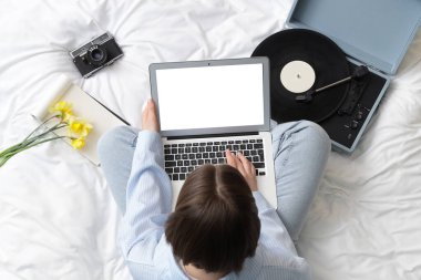 Pijamalı bir kadın boş dizüstü bilgisayar kullanıyor. Yatakta fotoğraf makinesi ve pikabı var.