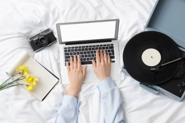 Yatakta fotoğraf makinesi ve pikabı olan dizüstü bilgisayarı kullanan kadın eller, üst görünüm.