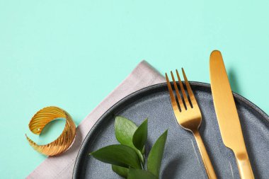 Altın çatal bıçak takımı ve turkuaz arka planda taze yapraklarla güzel bir masa.