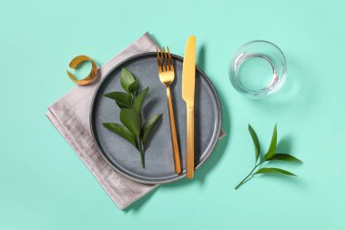 Altın çatal bıçak takımı ve turkuaz arka planda taze yapraklarla güzel bir masa.
