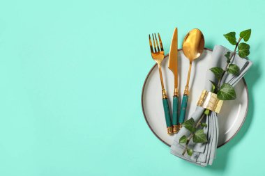 Altın çatal bıçak takımı ve turkuaz arka planda ağaç dalı olan güzel bir masa.