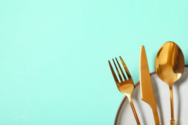 Turkuaz arka planda altın çatal bıçak seti olan güzel bir masa.