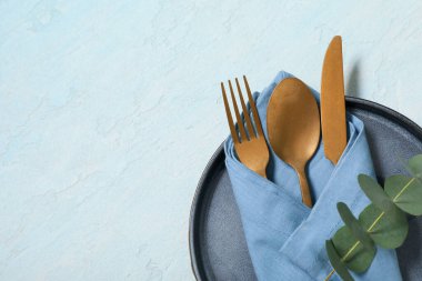 Altın çatal bıçak takımı ve açık mavi arka planda okaliptüs dallarıyla güzel bir masa.